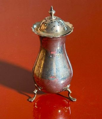 a silver vase with a lid on a red surface