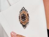 une femme vêtue d'un blazer blanc, avec une broche noire et dorée à la revers