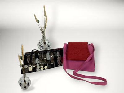 un sac à main rose avec une bandoulière rouge à côté, ainsi qu'un vase argenté avec des fleurs