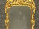un miroir à cadre doré posé sur un sol noir, près d'un mur