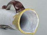 a white vase with a brown handle hanging on a wall