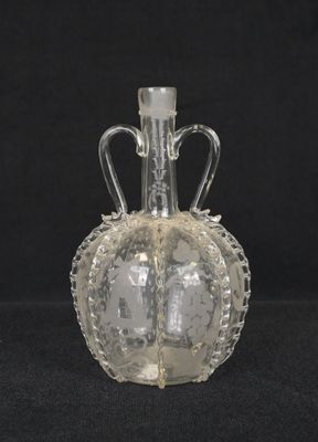 une bouteille en verre transparent munie d'une anse, sur fond noir