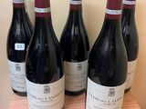 six bottles of red wine are lined up on a wooden table