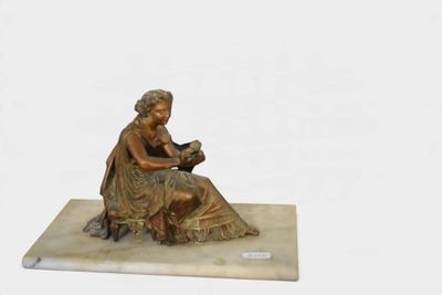 une statue représentant une femme en train de lire un livre, posée sur un socle en marbre