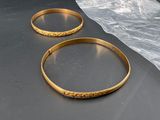 two gold bracelets sitting on a table next to a plastic bag