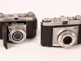two old cameras sitting side by side on a white surface