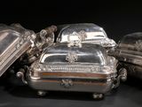 silverplated dishes and covers on a black surface with a black background