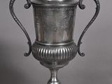silver plated urn with ornate handles on pedestal on grey background