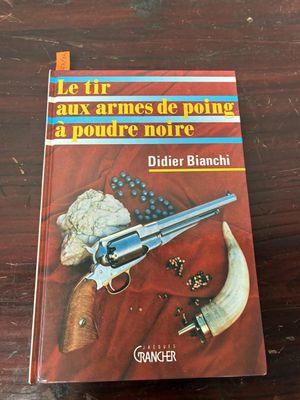 le livre est posé sur une table en bois, à côté d'un couteau et d'un pistolet