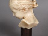 a white marble bust of a woman with braid hair on a wooden stand