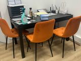 une table noire avec des chaises orange et un ordinateur portable posé dessus