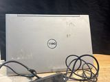 un ordinateur portable Dell posé sur une table en bois, avec son chargeur branché