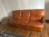 a brown leather couch in a living room with a blue rug