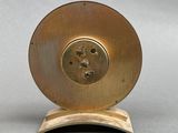 a gold clock on a wooden stand on a gray surface