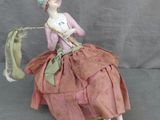 une figurine représentant une femme en robe rose et chapeau, assise sur une chaise