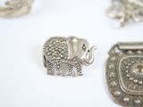 a silver elephant brooch on a table with other silver items