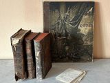 trois vieux livres posés sur une table à côté d'un tableau