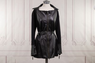 un manteau en cuir noir posé sur un mannequin devant un mur blanc