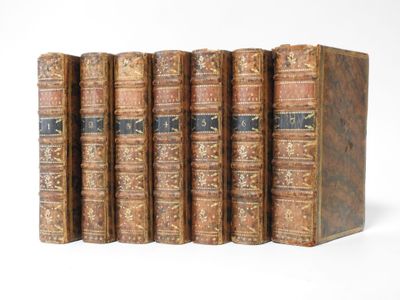 six old books are lined up in a row on a white surface