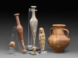 Plusieurs vases anciens et d'autres objets sont exposés sur un socle gris.