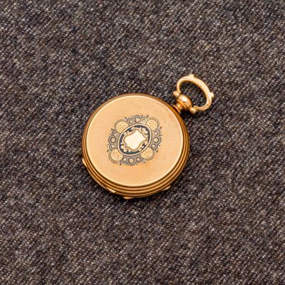 une petite montre de poche en or posée sur un tissu gris