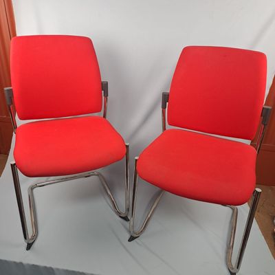 pair of red office chairs with chrome legs and arms