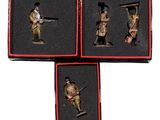 trois figurines miniatures de soldats dans des boîtes rouges posées sur une surface blanche