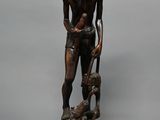 statue en bois représentant un homme coiffé d'un chapeau, accompagné d'un chien, assis sur un rocher