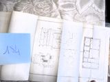 une pile de papiers posée sur un lit, sur laquelle se trouve un post-it bleu