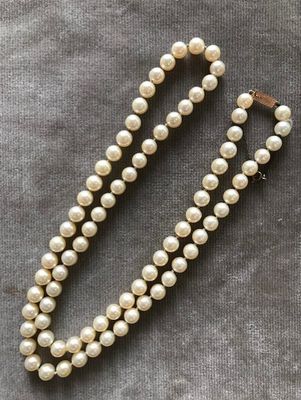 un collier de perles blanches muni d'un fermoir en or, sur fond gris