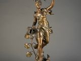 an antique bronze statue of a woman holding a fan and a flower