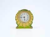 une petite horloge verte et dorée posée sur une surface blanche
