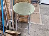 un tabouret vert posé à côté d'une pile de balais