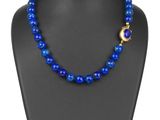 un collier de perles bleues muni d'un fermoir doré, posé sur un mannequin