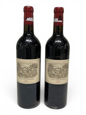 two bottles of red wine sitting next to each other on a white surface