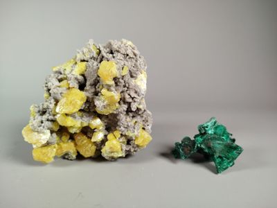 yellow and green crystals on a white surface next to a green piece of rock