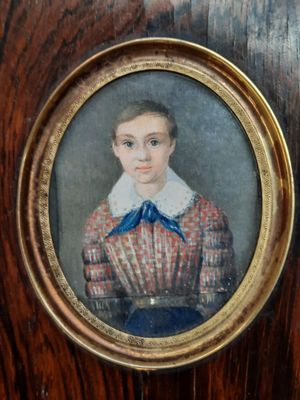 portrait d'un jeune garçon vêtu d'une robe rouge et blanche ornée d'un nœud bleu