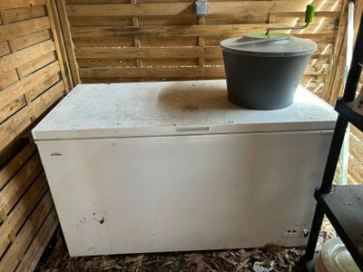 un réfrigérateur blanc posé dans une pièce, avec un seau posé dessus