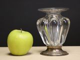 a green apple next to a glass vase on a table