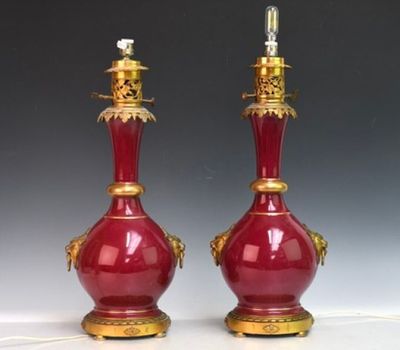 paire de vases rouges avec des bordures et des anses dorées sur un fond blanc