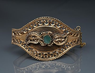 a close up of a gold bracelet with a green stone