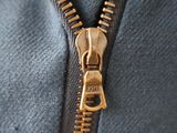 close up of a zipper on a blue jacket with a gold zipper