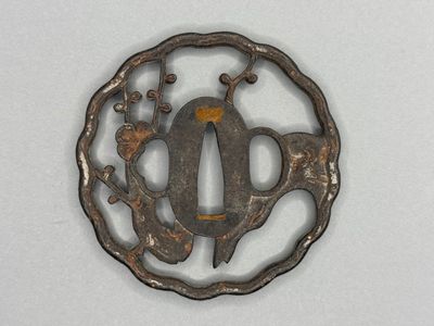 an old iron tsuba with a bird and flowers in the center