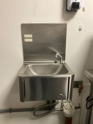 a stainless steel sink in a public restroom with a paper towel dispenser attached to the wall