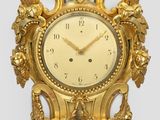 une horloge en or accrochée au mur, sur laquelle est représenté un oiseau