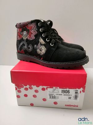 Les bottes noires des enfants sont posées sur une boîte rose.