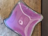 purple glass bowl sitting on top of a wooden table next to a knife