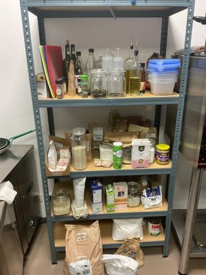 une étagère remplie de provisions dans une cuisine, à côté d'un réfrigérateur