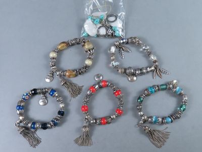six bracelets différents, ornés de pompons et de perles, posés sur une table