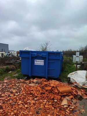 une benne bleue posée au milieu d'un tas de gravats